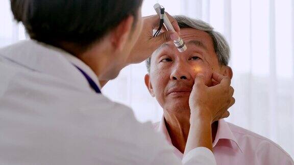 医生在医院用铅笔给病人检查眼睛资深的眼科医生在验眼仪中寻找一位老年男性的眼部症状医学教育、保健、技术、人与医学理念医疗咨询