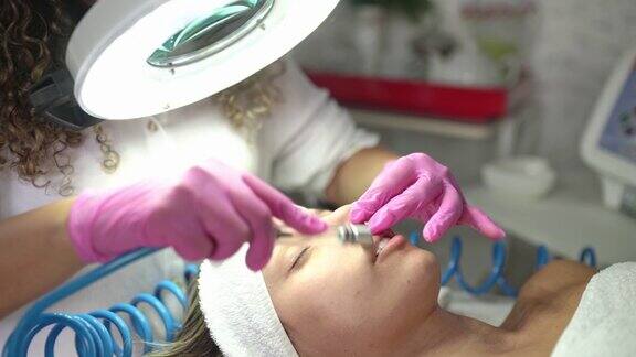 在一位女性客户的脸上做微磨皮治疗的美容师