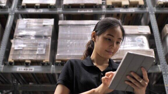 年轻愉快的女工人正在工厂的存储区使用她的平板电脑