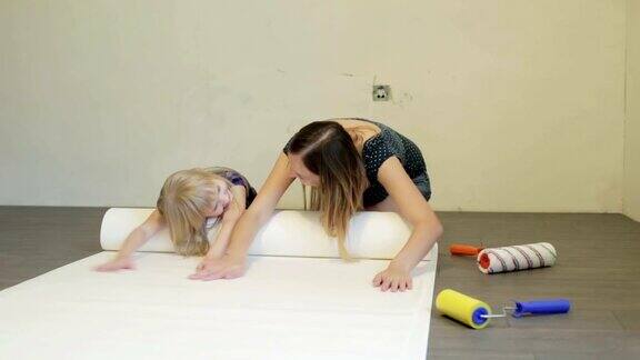 母亲和金发碧眼的小女儿正在擦拭地板上的白色墙纸