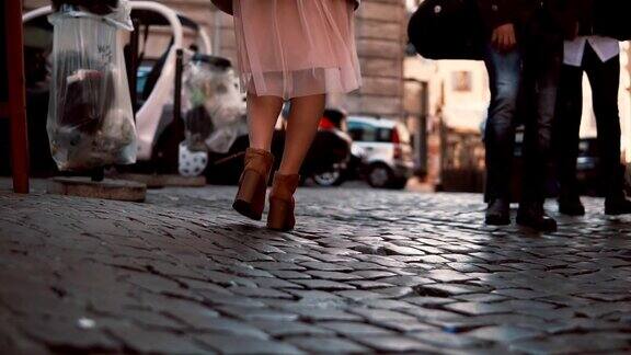 女人走在城市的鹅卵石人行道上女孩穿着高跟鞋和裙子探索城镇特写镜头