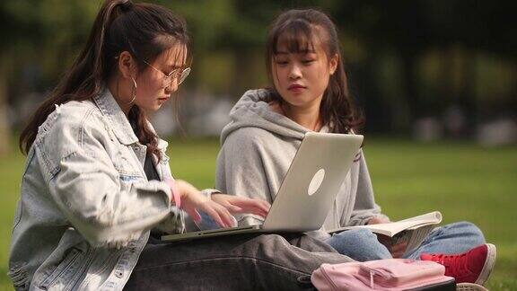 两个女大学生坐在校园的草坪上学习