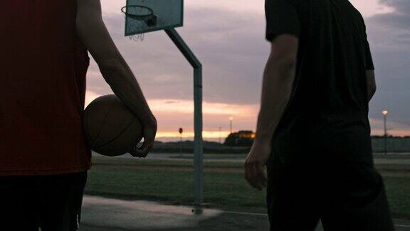 黄昏时分年轻人走出户外篮球场两个朋友在室外打篮球