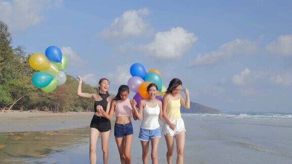 一群女朋友在蓝天的映衬下拿着气球在沙滩上散步在夏日阳光明媚的阳光下朋友们在沙滩上嬉戏假期iStock