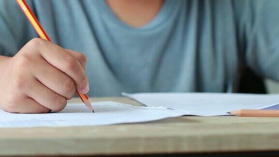 教育考试在大学或高中:手持铅笔的学生测试试卷上的答案在校园教室填写试卷知识学习