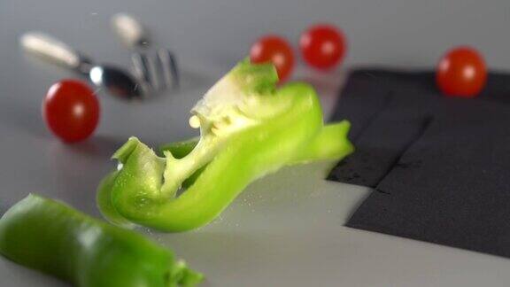 一片片绿色的甜椒落在灰色的背景上用勺子、叉子、樱桃番茄和三张黑色的餐巾做成的静物