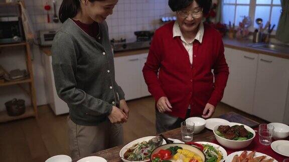 快乐的亚洲老婆婆穿着红色的衣服看着女儿在餐桌上端着汤准备在家里吃团圆饭关于内阁翻译的“财富”字