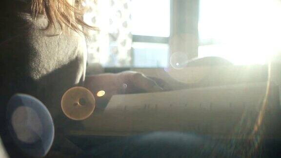 年轻女子在傍晚的阳光下坐在窗边看书