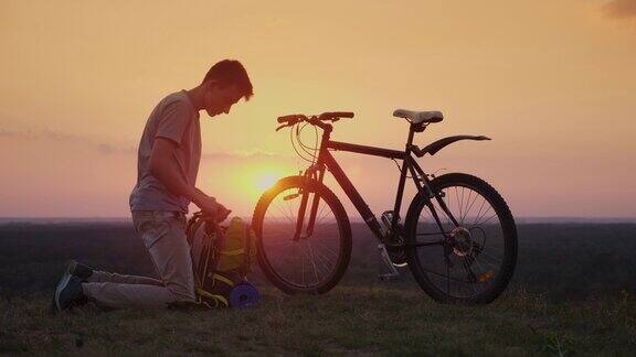 一个年轻人把东西放在背包里日落时坐在自行车旁
