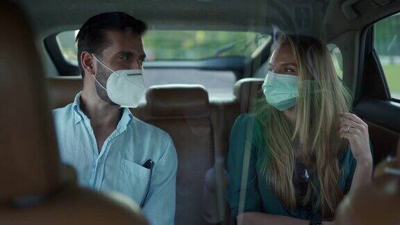 一名男子和一名女子戴着防护面罩坐在出租车后座上聊天享受旅程