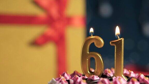 61号生日蛋糕用金色蜡烛点燃蓝色背景的礼物用红丝带绑在黄色盒子里特写和慢动作