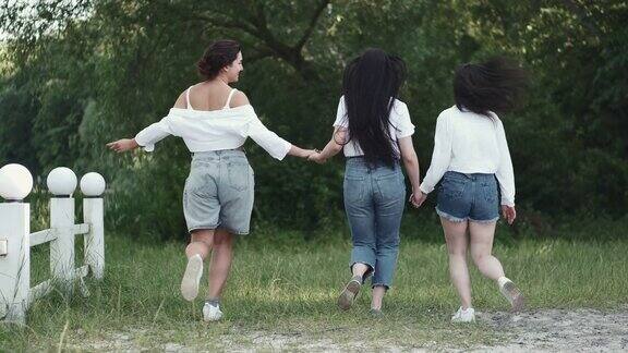 三个漂亮的黑发女友手牵着手在草地上散步
