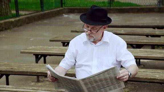戴着帽子的帅老头在公园的长椅上读报纸