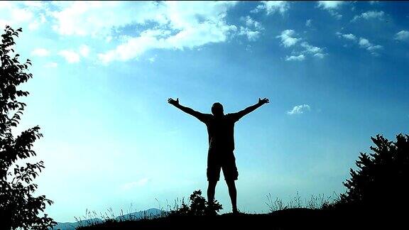 一个年轻人站在山顶举起双手象征着成功、成功和快乐概念和象征成功、好运、成就、繁荣