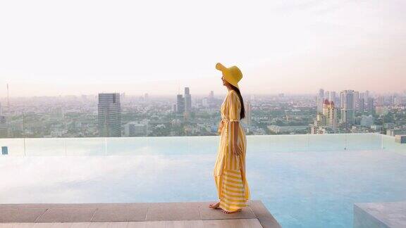 美丽的照片亚洲妇女在一个黄色的长裙和黄色的大帽子走在池边在多彩的日落女孩享受暑假与美丽的日落和城市的光线