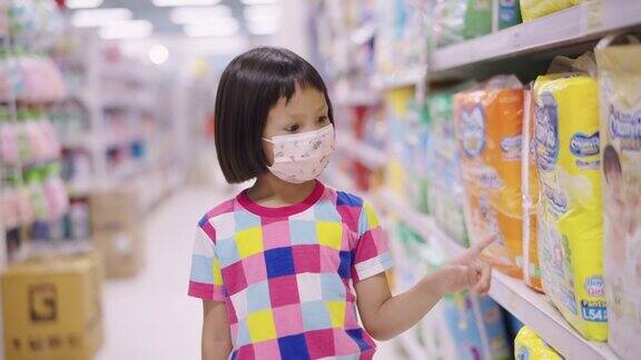 一个亚洲小女孩戴着口罩在当地的超市里走着看着货架上的产品