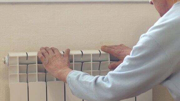 一位白人老人摸着暖气片检查室内温度房间的热调节一位老人呆在家里等待暖气供应