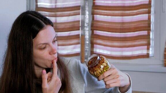 一个女人用手指从一个罐子里拿坚果吃蜂蜜