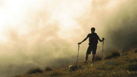 一个年轻的徒步者背着背包穿着靴子拄着拐杖站在迷雾中的山上云和迷雾在背景上移动意大利阿布鲁佐