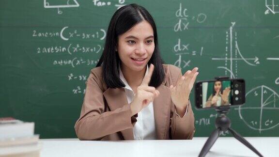 年轻的亚洲女教师坐在和学生视频会议女教师在课堂上通过智能手机在线课程直播培训数学
