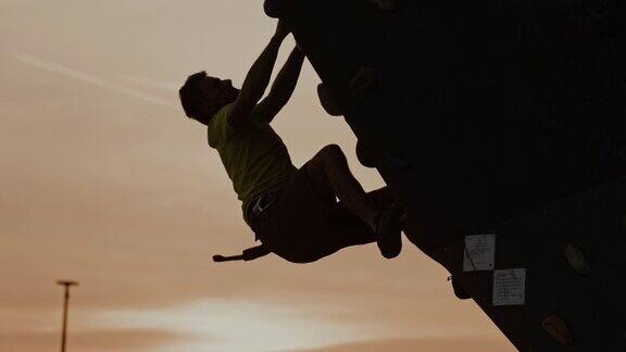 黄昏时分一名登山者试图抓住户外攀岩墙时摔倒