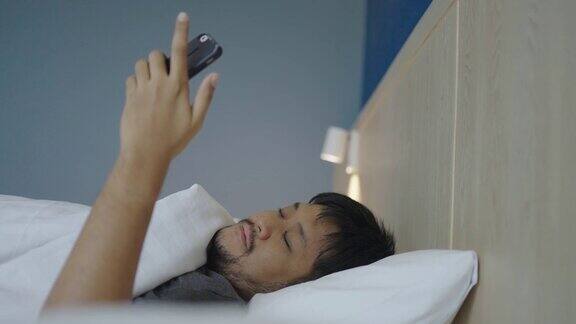 早上一个亚洲男人仰面躺在床上用手机打呵欠