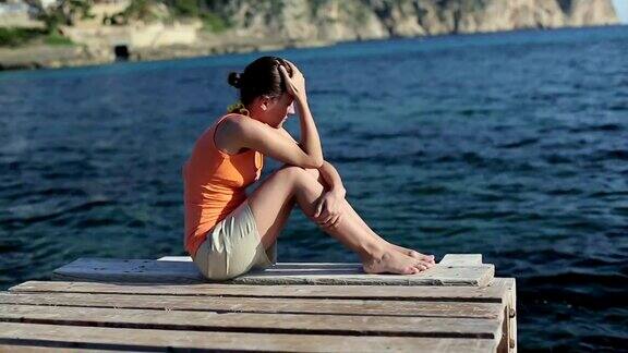 悲伤的女人坐在海边的码头上跟踪拍摄