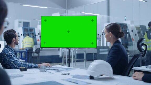 现代工厂办公室会议室:多样化的工程师经理和投资者团队在会议桌上交谈观看互动电视显示绿屏色度键模拟