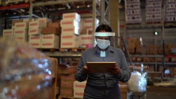 女工在仓库边行走边使用平板电脑戴着口罩