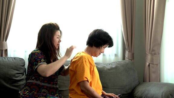 女儿教她妈妈在家里的沙发上使用放松按摩设备