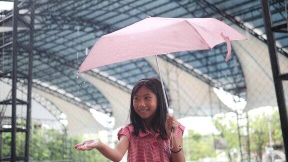 亚洲女孩拿着粉红色的伞在大雨中捕捉雨滴的慢动作