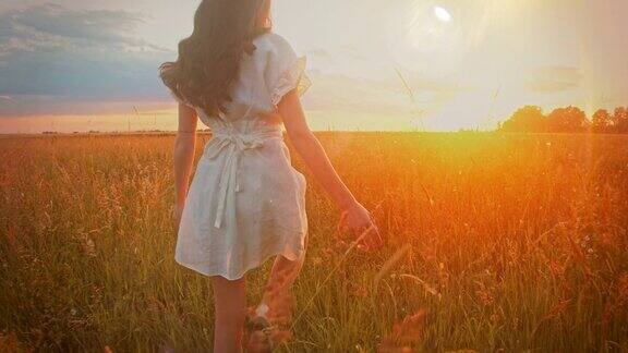 一个穿着白色裙子的女人在日落时走在草地上的美丽镜头