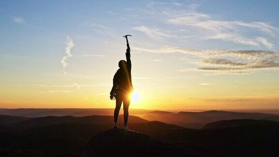 一位年轻的女登山者在夕阳下站在山顶上胜利地举起双手