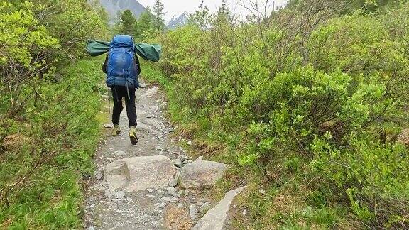 一个背着大背包的游客独自走在森林里的一条岩石小道上徒步到白露哈山顶