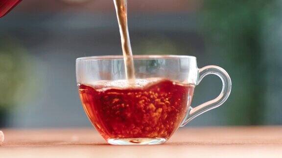 特写镜头将流着新鲜香气的热红茶倒入透明玻璃杯茶壶上桌