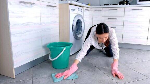 戴着粉色橡胶手套的女人用一块布擦洗厨房地板