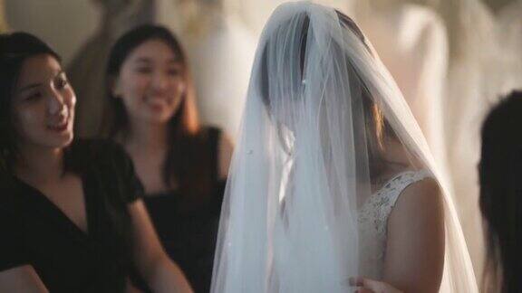 亚洲的中国新娘在婚纱店试穿婚纱伴娘在旁边欣赏婚纱的美丽