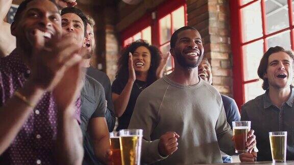 一群男性和女性朋友庆祝同时在体育酒吧看屏幕上的游戏