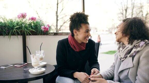 两个迷人的混血女人在街头咖啡馆边喝咖啡边聊天朋友们参观商场后玩得很开心