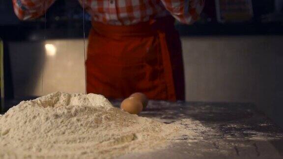在披萨店的厨房里厨师把一个鸡蛋扔在一堆面粉上