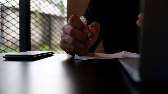 男人在纸上写字工作时使用智能手机