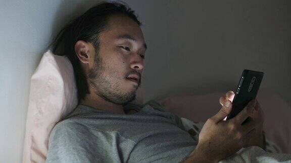 近距离的亚洲男子斗争而使用智能手机在床上晚上