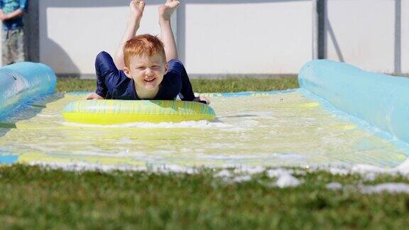 可爱的红发男孩在夏天玩滑水道