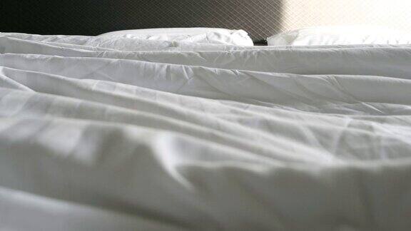 皱巴巴的白色毯子两个枕头早上起床后没有整理的床上有羽绒被