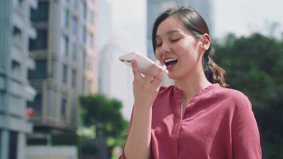 亚洲女性在公园里用智能手机上的语音助手为朋友聊天