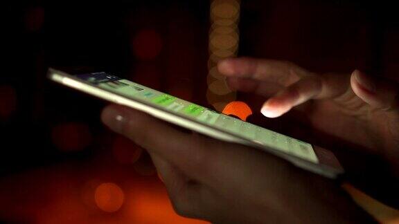 女人的手使用智能手机触摸屏的特写在夜晚的城市户外输入消息