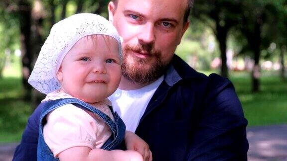 年轻的爸爸抱着女儿在城市公园全家福看着相机