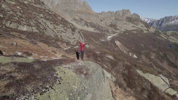 无人机拍摄的一个女人在被山脉包围的山顶上做自由的姿势