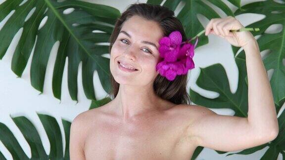 年轻美丽的女人皮肤光滑手持兰花背景是热带树叶