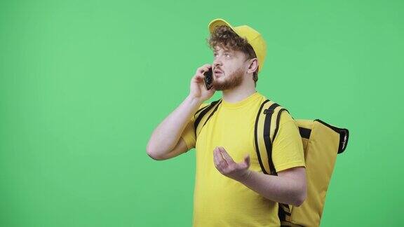 年轻男子的肖像说话的电话指定送货地址红发男穿着黄色快递制服带着保温袋在绿色屏幕上摆姿势关闭了慢动作准备59.97fps